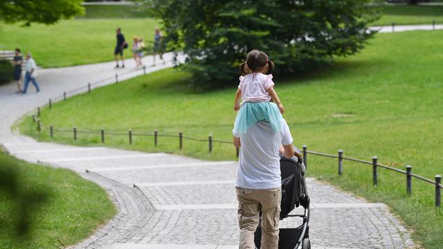 Father carries his daughter on his shoulders and pushes a stroller.