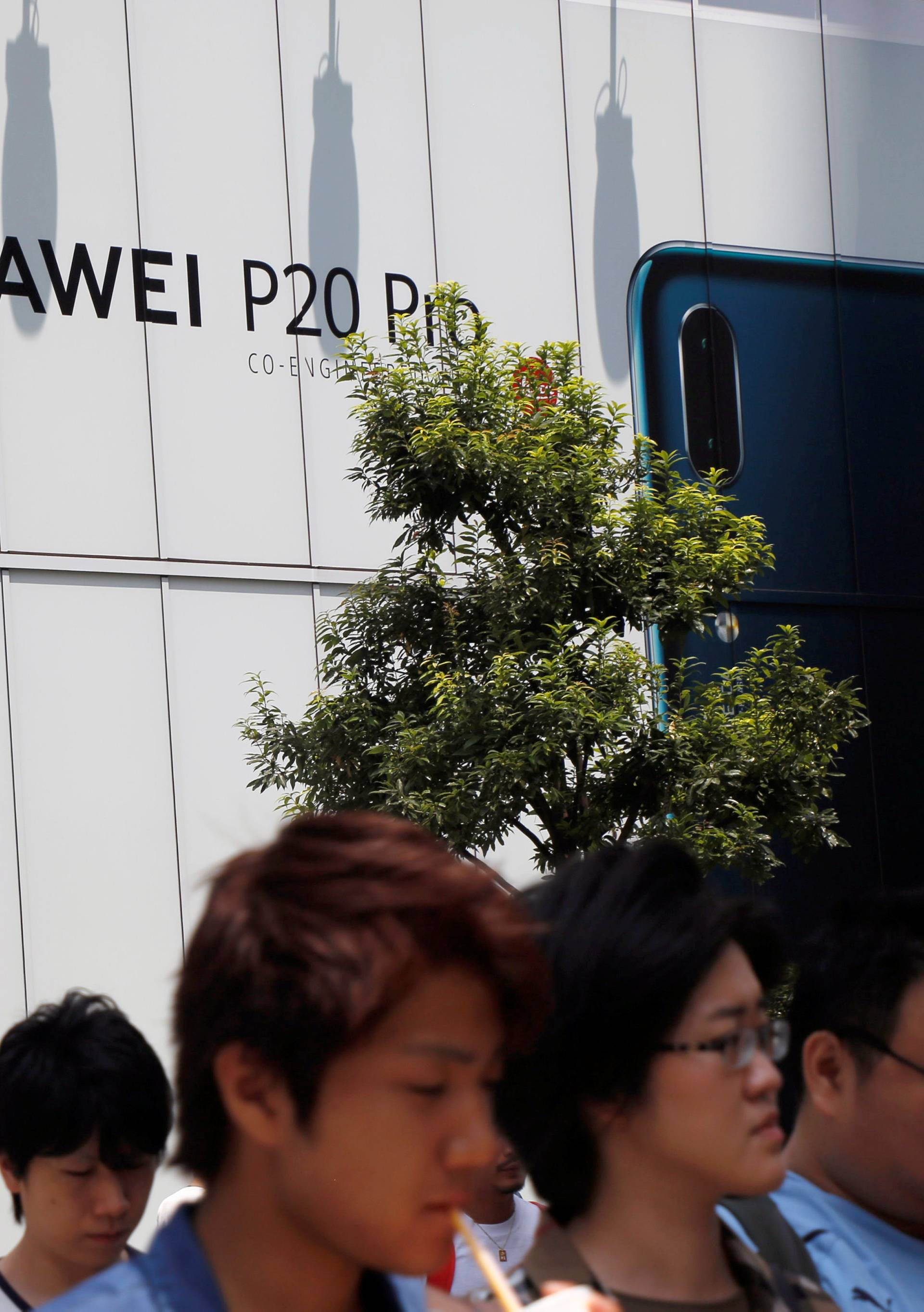 People walk past an advertisement for Huawei outside an electronic store in Tokyo