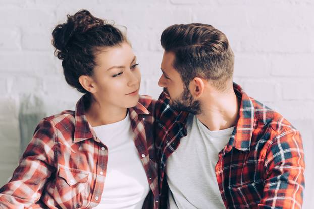 joyful young woman in checkered shirt embracing boyfriend at home