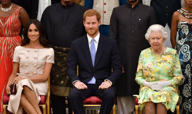 FILE PHOTO: Britain's Queen Elizabeth, Prince Harry and Meghan, the Duchess of Sussex pose for a picture with some of Queen's Young Leaders at a Buckingham Palace reception following the final Queen's Young Leaders Awards Ceremony, in London