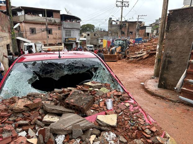 People observe as rescue workers search for people among the debris of a house that collapsed due to heavy rains, in Juiz de Fora