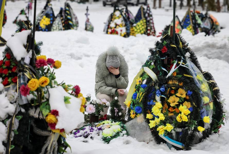 A woman reacts as she sits in front of a grave at a local cemetery, decorated with flowers to pay tribute to the victims of the Russian attack on Ukraine, in Chernihiv