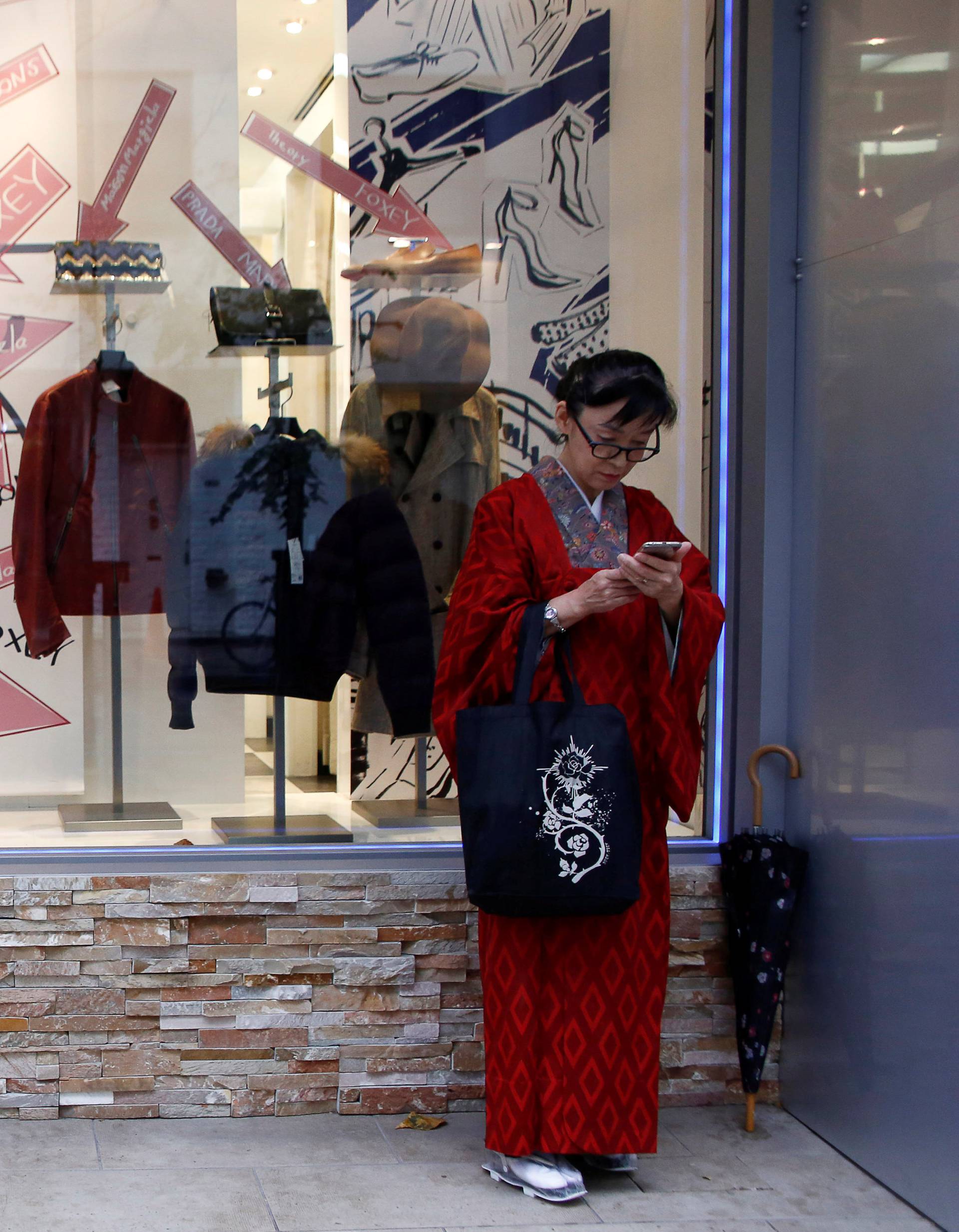 A woman wearing a traditional costume stands in front of a shop window at a shopping district in Tokyo