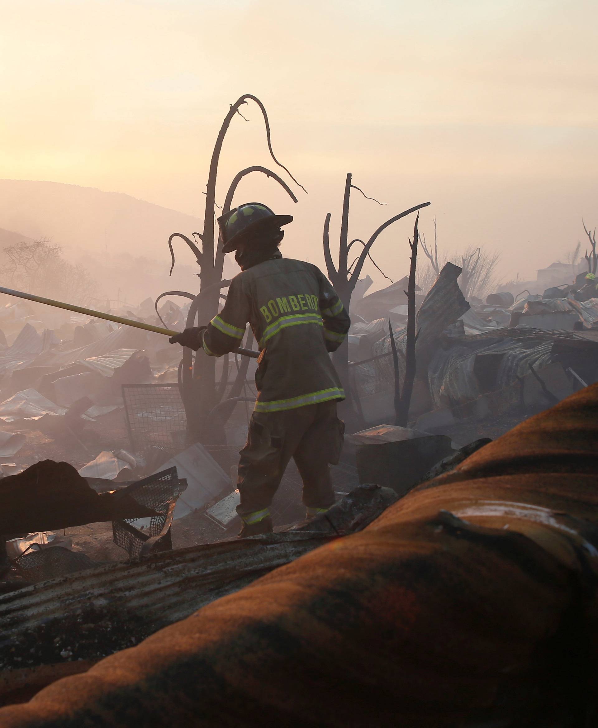 A firefighter removes the remains of a burned house on a hill, where more than 100 homes were burned due to forest fire but there have been no reports of death, local authorities said in Valparaiso, Chile