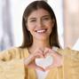 Cheerful beautiful young woman keeping finger heart at chest