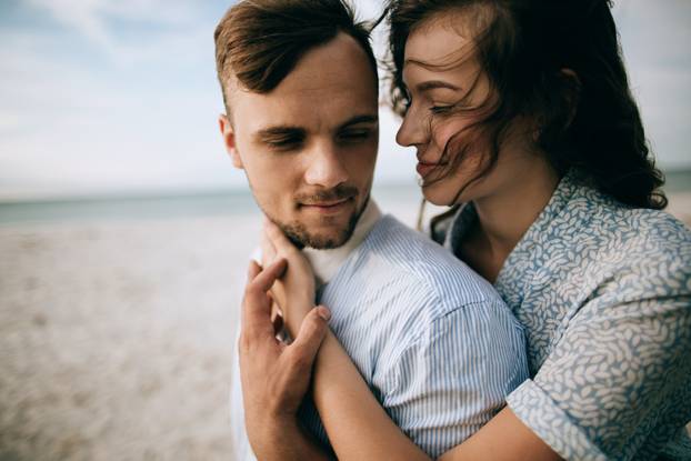 Young woman tenderly hugs her boyfriend on the sea beach. The co