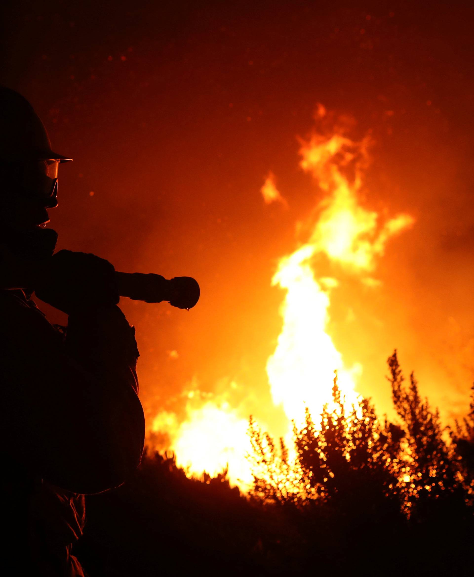 A firefighter works at the top of a hill as the Lilac Fire burns through Bonsall, California