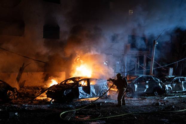 An Israeli firefighter works to put out a fire on a car at the site of a projectile impact, in Tel Aviv