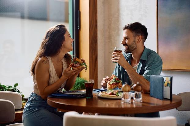 Young,Happy,Couple,Eating,Pizza,And,Talking,In,A,Restaurant.