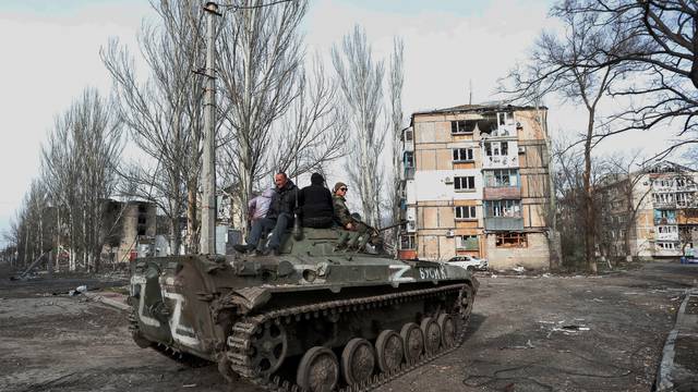 Service members of pro-Russian troops and civilians sit atop of an armoured vehicle in Mariupol