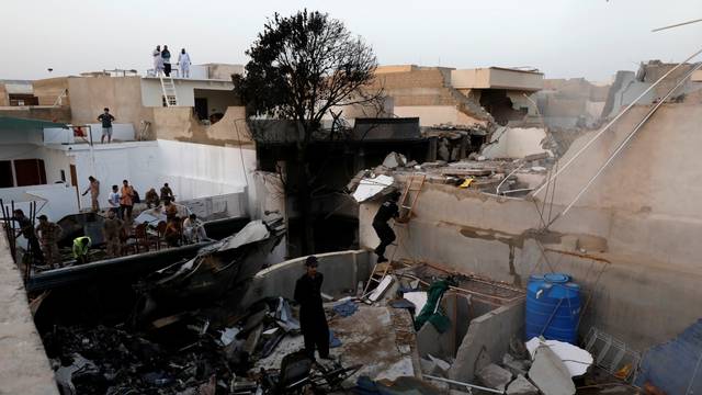 People stand on a roof of a house amidst debris of a passenger plane, crashed in a residential area near an airport in Karachi