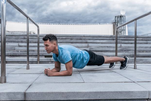 Male athlete standing in the bar, training the muscles of the abdominal cortex and abs, in the summer in the city, strength and concentration for a while. Fitness in the city, active lifestyle.