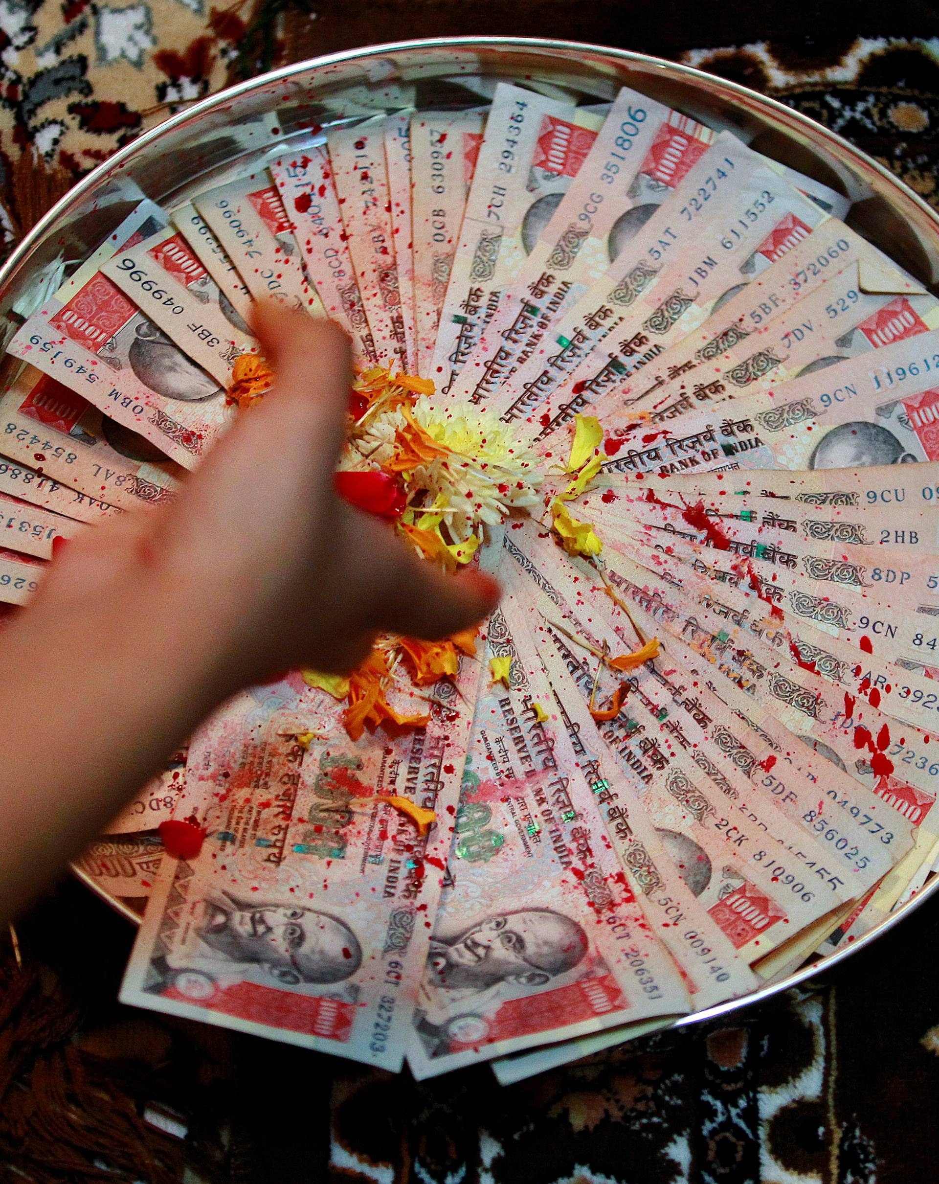 A woman puts flower petals on 1000 Indian rupee notes as she prays as part of a ritual during Dhanteras in Ahmedabad