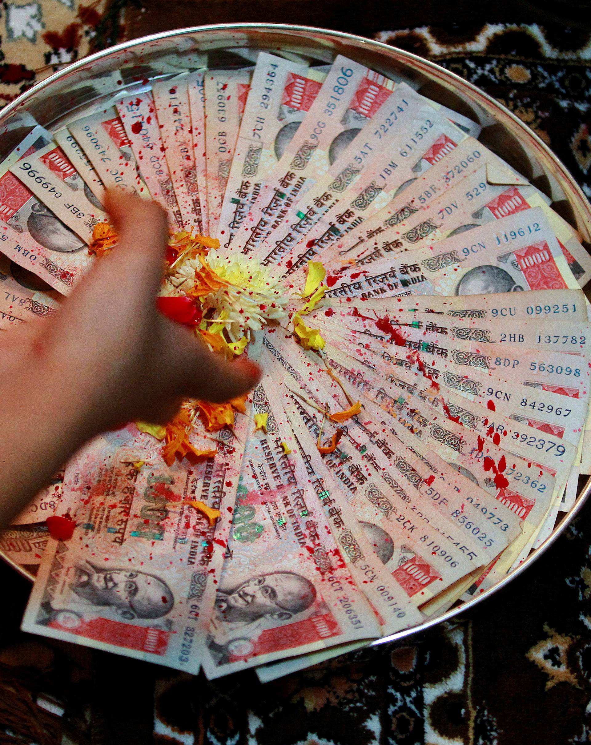 A woman puts flower petals on 1000 Indian rupee notes as she prays as part of a ritual during Dhanteras in Ahmedabad