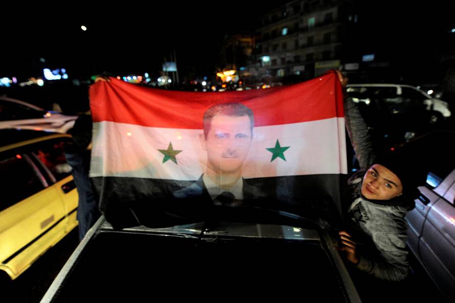 Supporters of Syria's President Bashar al-Assad carry a Syrian national flag with his picture as they tour the streets in celebration of what they say is the Syrian army's victory against the rebels in Aleppo