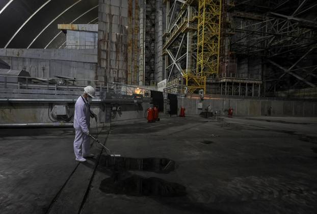 An employee measures a radiation level to the old sarcophagus covering the damaged fourth reactor, under the New Safe Confinement structure at the Chornobyl Nuclear Power Plant