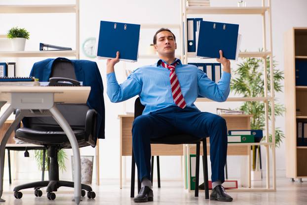 Young male employee doing sport exercises at workplace