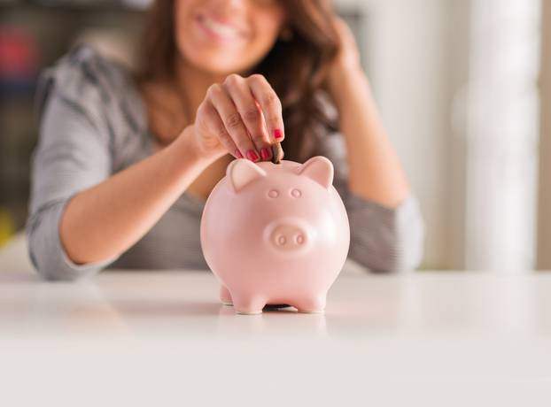 Woman,Putting,Coin,In,Piggy,Bank,,Indoors