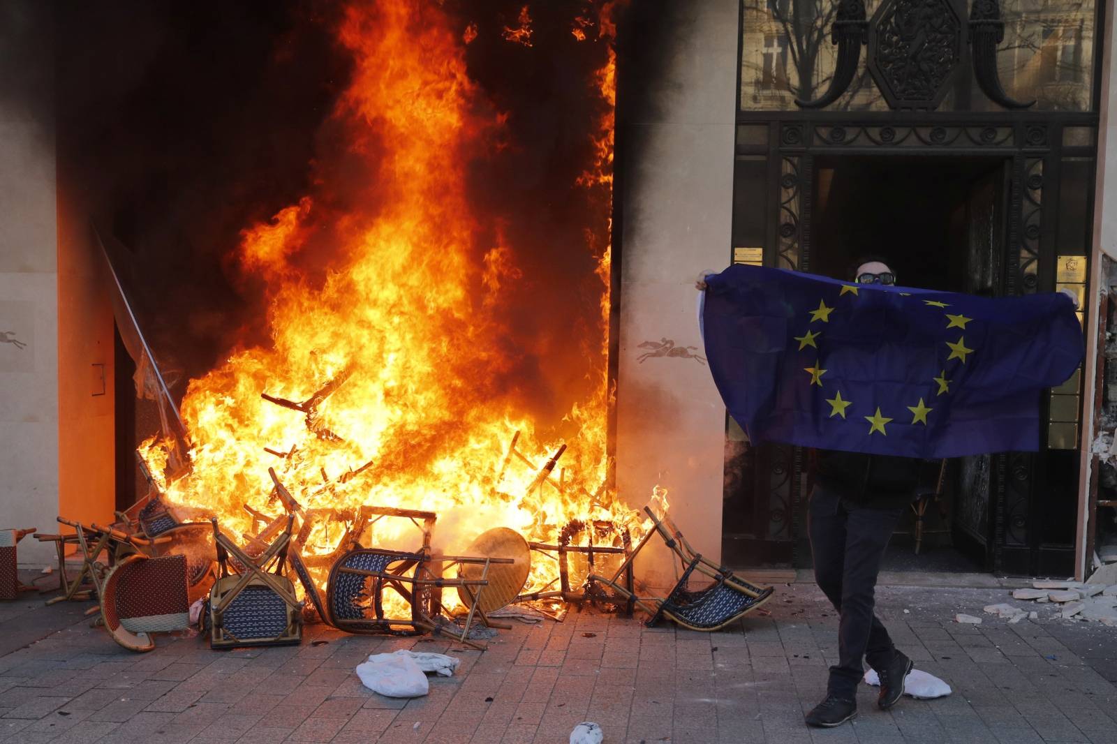 A demonstrator holds European flag near burning shop during demonstration by "yellow vests" in Paris