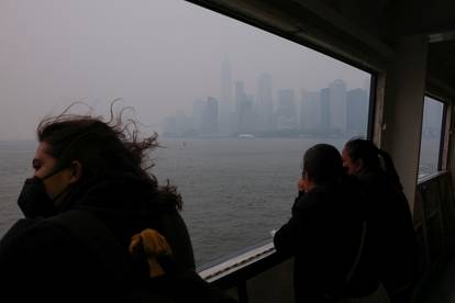 A commuter wearing a face mask stands on the Staten Island Ferry while the Manhattan skyline is seen in the background covered by haze and smoke caused by wildfires in Canada, in New York
