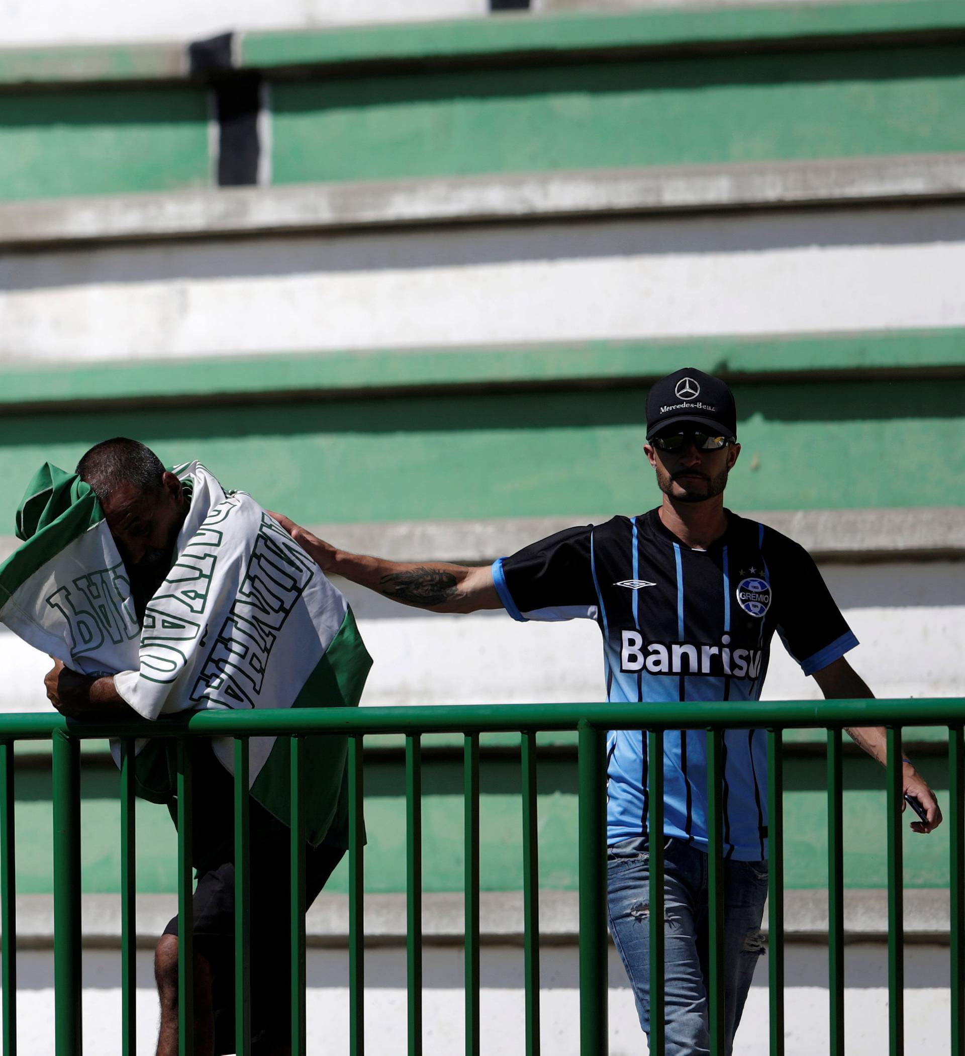A soccer fan wearing a jersey of Gremio soccer club comforts a fan of Chapecoense soccer team reacting at the Arena Conda stadium in Chapeco