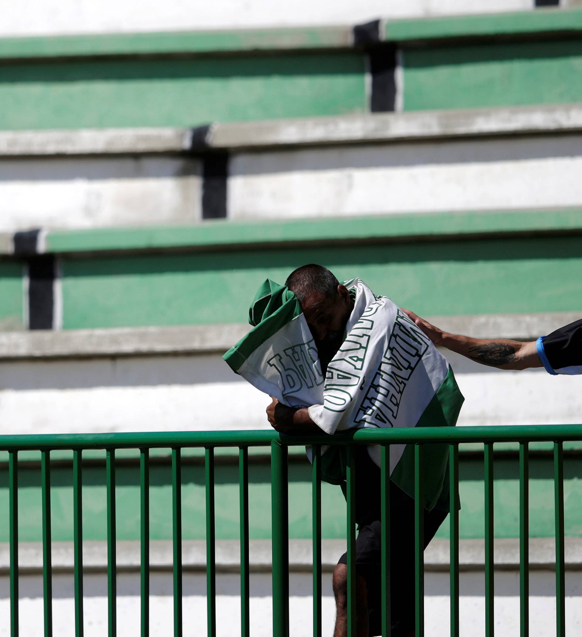 A soccer fan wearing a jersey of Gremio soccer club comforts a fan of Chapecoense soccer team reacting at the Arena Conda stadium in Chapeco