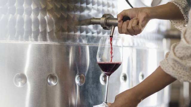 Vintner barrel tasting red wine from stainless steel vat