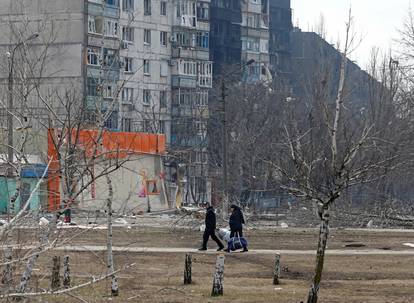 Local residents walk near a damaged residential building in the besieged city of Mariupol