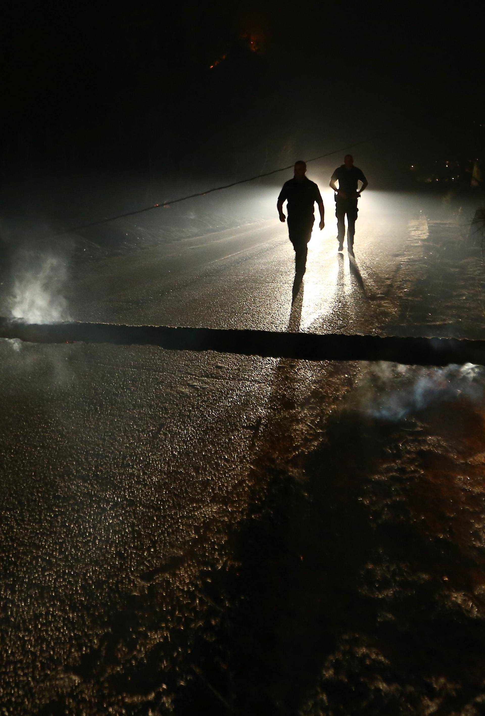 Local residents walk on the blocked road by timber,  burned by wildfire in the village of Mravince near Split