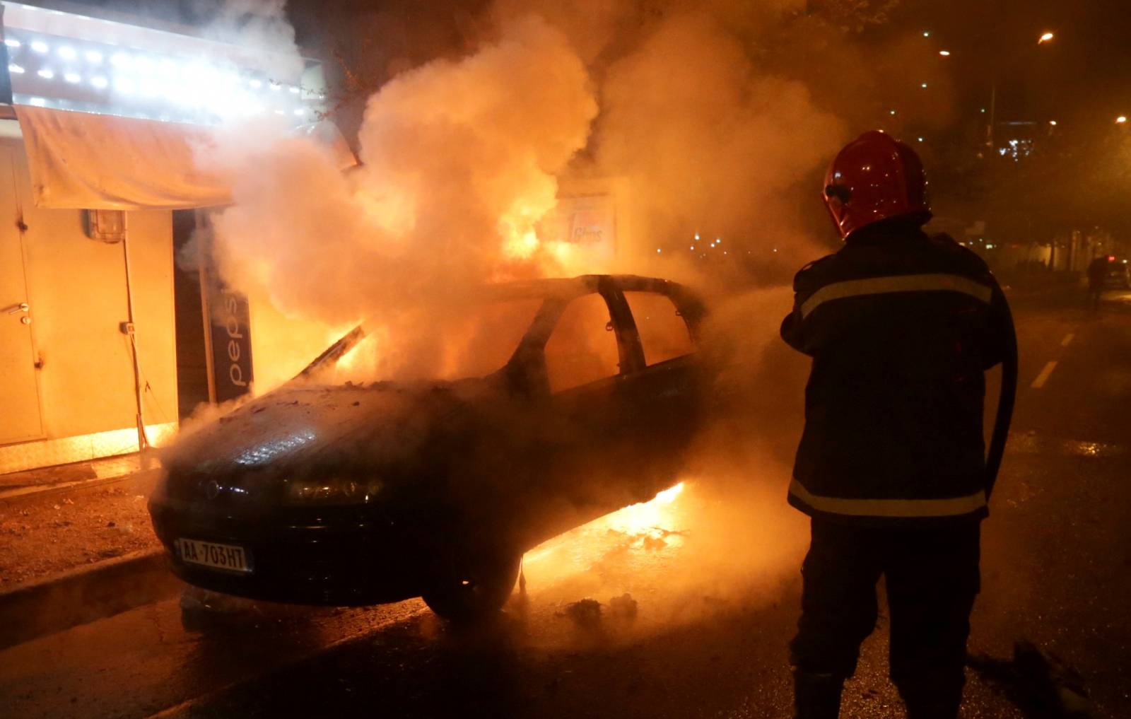 A firefighter extinguishes a burning car during an anti-government protest near the Parliament Building in Tirana