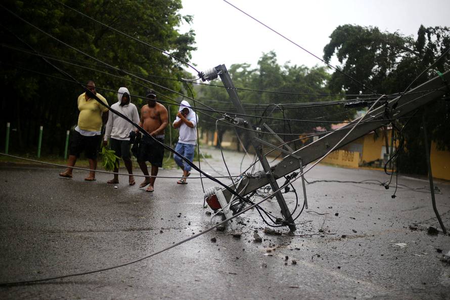 Locals walk past a fallen power pole as Hurricane Irma moves off the northern coast of the Dominican Republic, in Puerto Plata