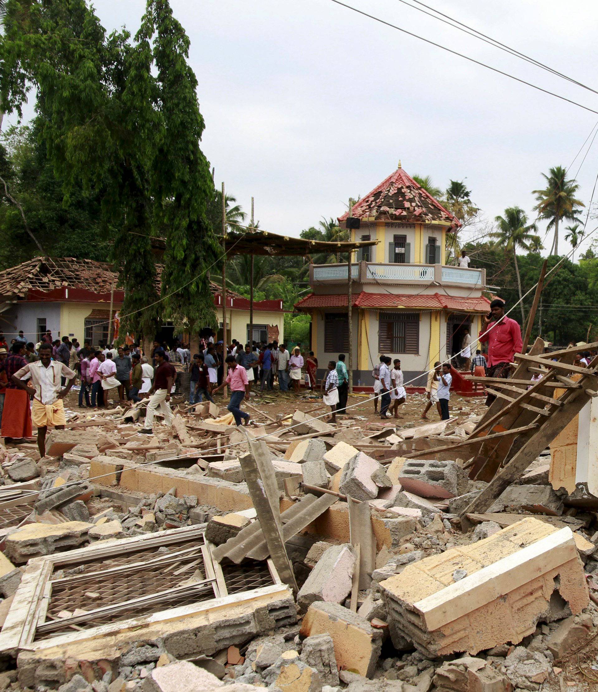 People walk past debris after a fire broke out at a temple in Kollam in the southern state of Kerala