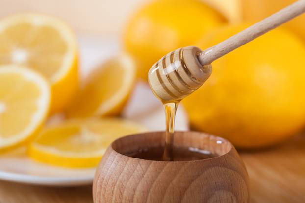 honey in a wooden bowl with honey dipper and lemon on a wooden k