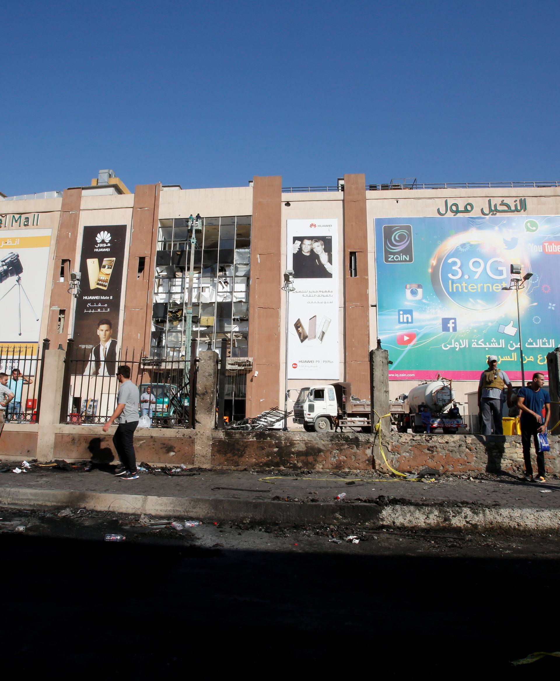 People walk past the site of a suicide bomb attack at Nakheel Mall across from the oil ministry in Baghdad