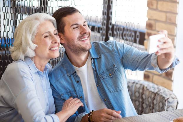 Joyful woman and her adult grandson making selfies