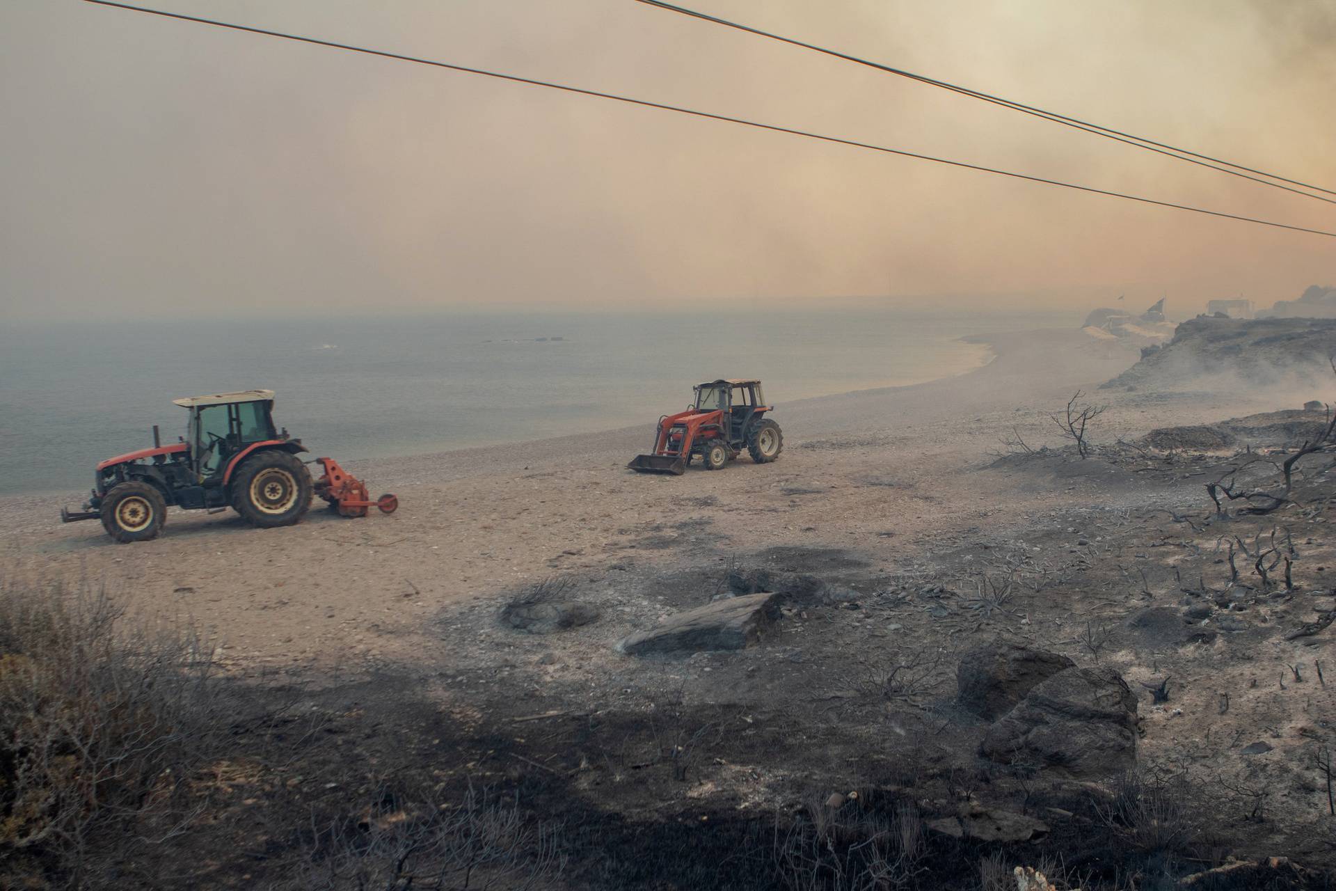 An empty beach is pictured amidst smoke rising from wildfire burning near Lindos, on the island of Rhodes