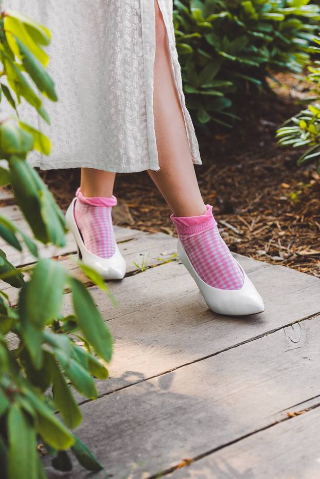 low section of girl in dress and stylish white shoes walking on wooden walkway