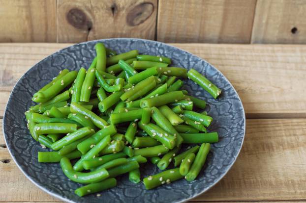 Plate with cooked green beans on wooden background