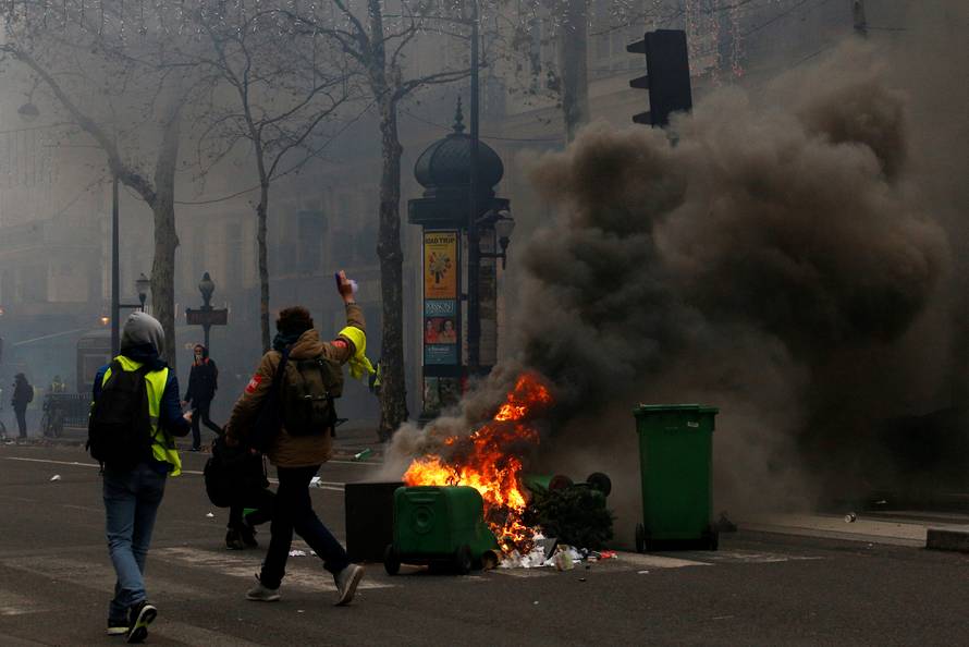Protesters wearing yellow vests walk past burning trash bins during clashes with police at a demonstration during a national day of protest by the "yellow vests" movement in Paris