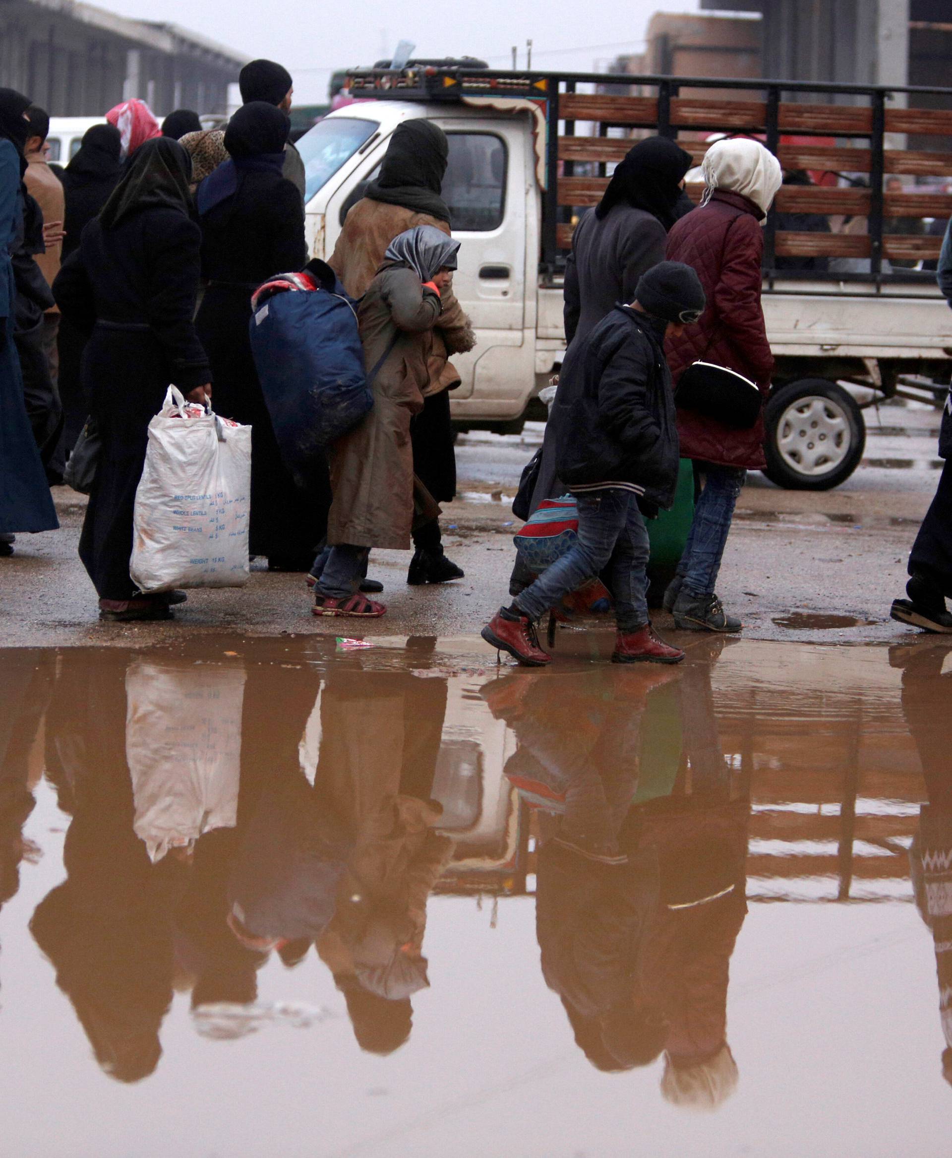 Syrians evacuated from eastern Aleppo walk with their belongings near a puddle of water in government controlled Jibreen area in Aleppo