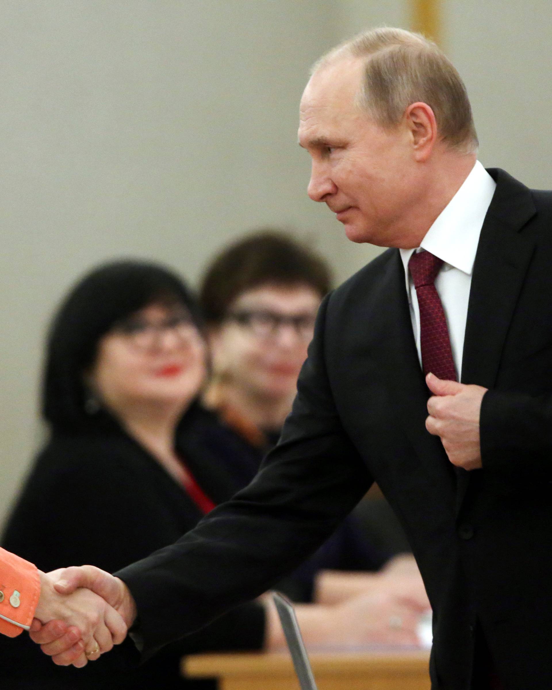 Russian President and Presidential candidate Vladimir Putin shakes hands with a member of a local election commission at a polling station during the presidential election in Moscow