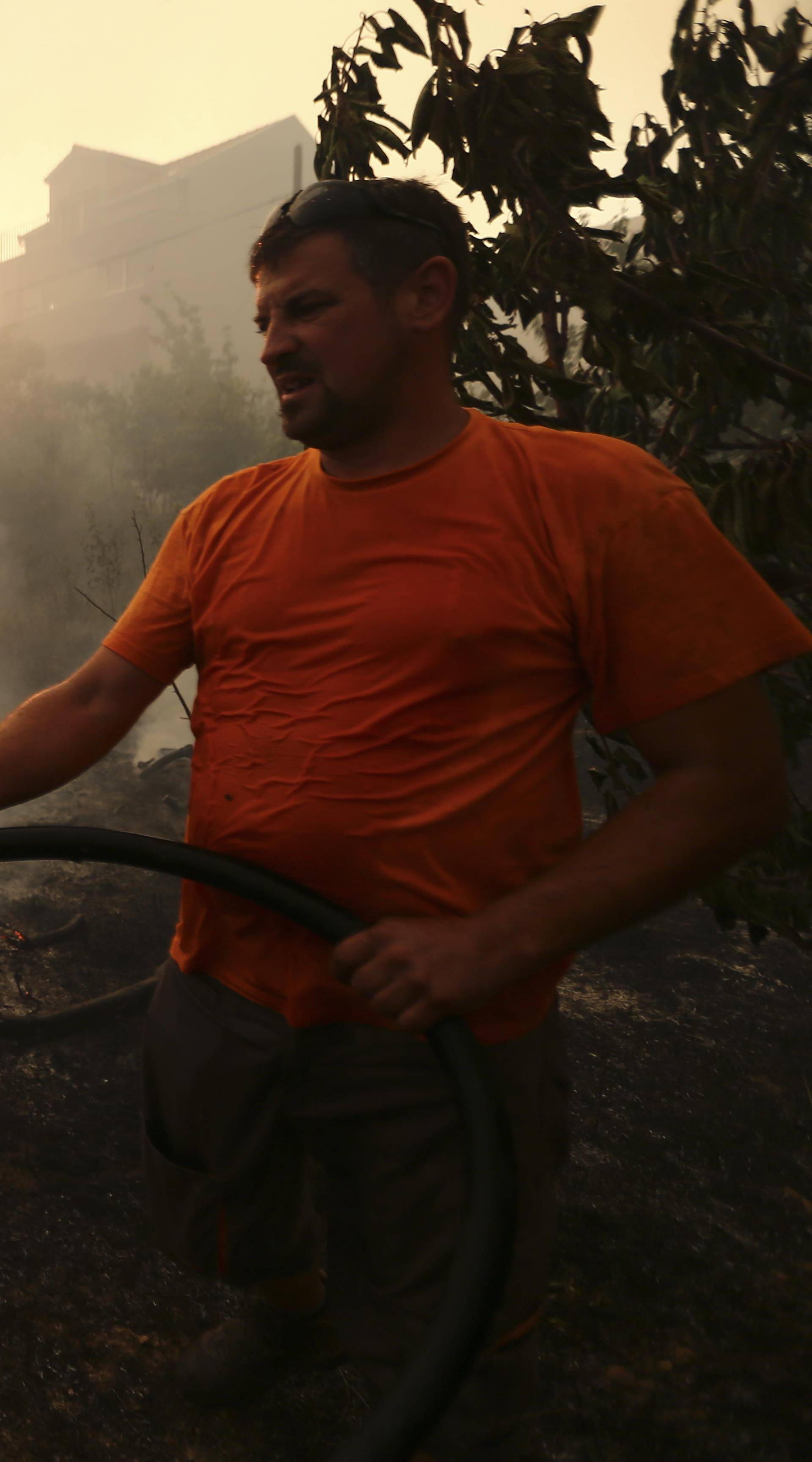 A local resident holds a hose as he tries to extinguish a wildfire in the village of Mravinc near Split