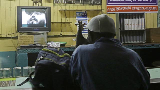 A man watches a television broadcast with the image of Cuba's former President Fidel Castro in Havana