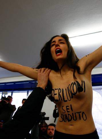 A topless activist of women's rights group Femen interrupts voting as Forza Italia party leader Silvio Berlusconi casts his vote at a polling station in Milan