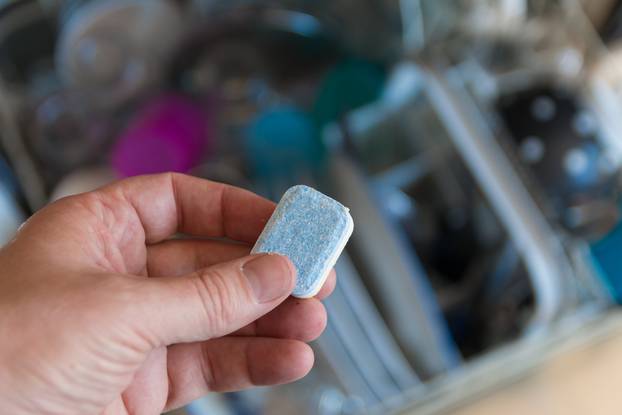 hand placing dishwasher tablet into dishwasher