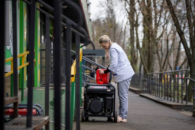 A woman fills petrol into a power generator to produce electricity for a pharmacy after critical civil infrastructure was hit by a recent Russian missile and drone attack in Kyiv