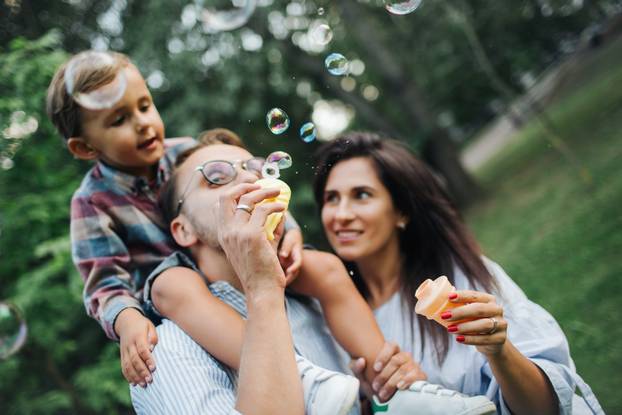 Happy young family playing with bubble wands in park outdoors