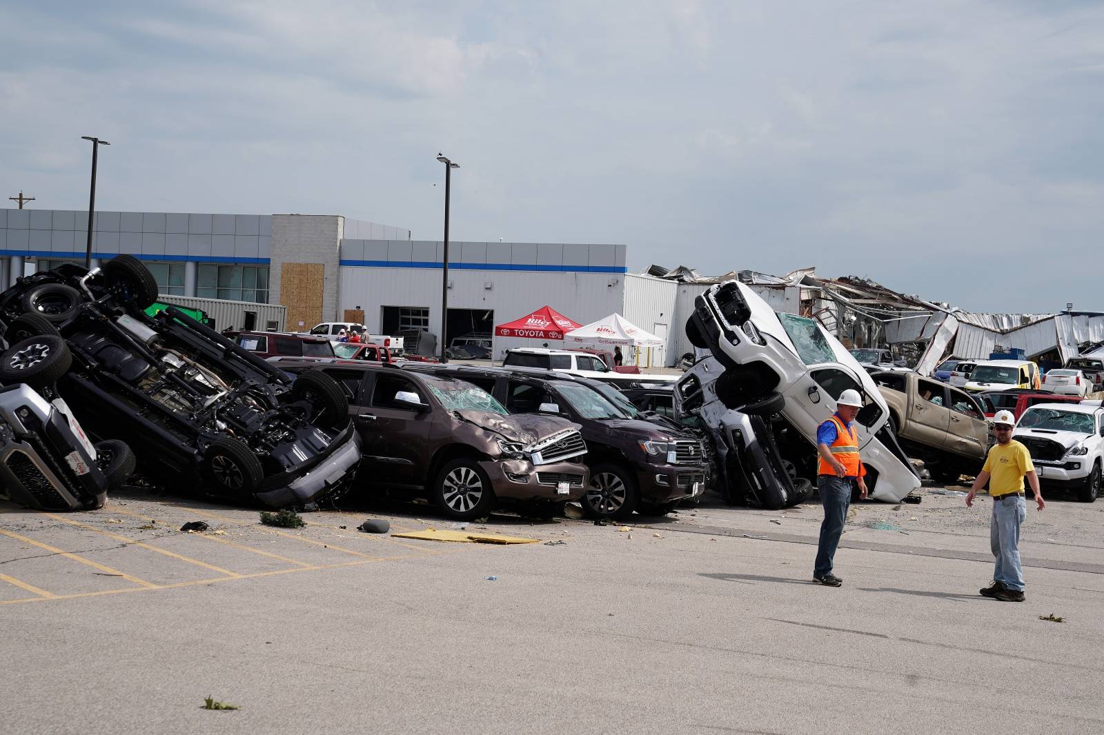 Workers walk past wrecked trucks at a Toyota dealer following a tornado in Jefferson City