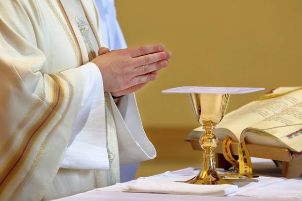 Chalice on the altar and priest celebrating mass in the background and empty space for text