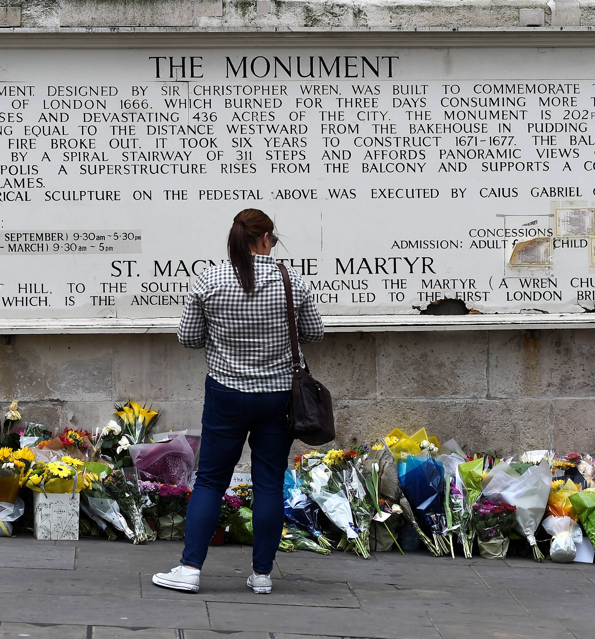 A woman observes flowers left along the base of the Monument to the Great Fire of London near London Bridge after an attack on the bridge and nearby Borough Market left 7 dead and dozens injured, in London